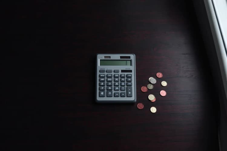 Uma calculadora e moedas de dinheiro espalhadas sobre uma superfície de madeira escura, representando custos de campanha.
