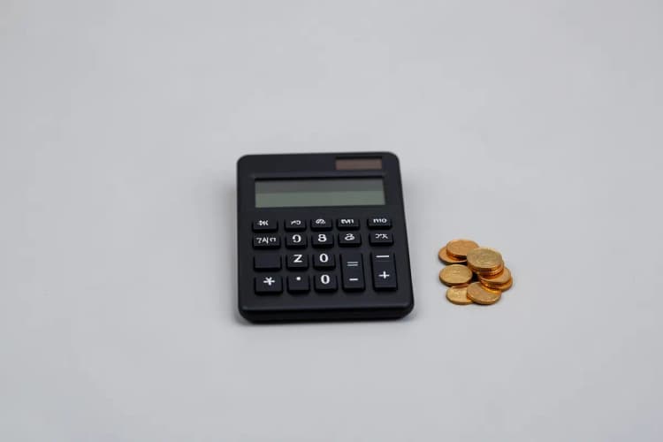 Uma mão segurando uma calculadora e moedas, com um gráfico desfocado ao fundo.