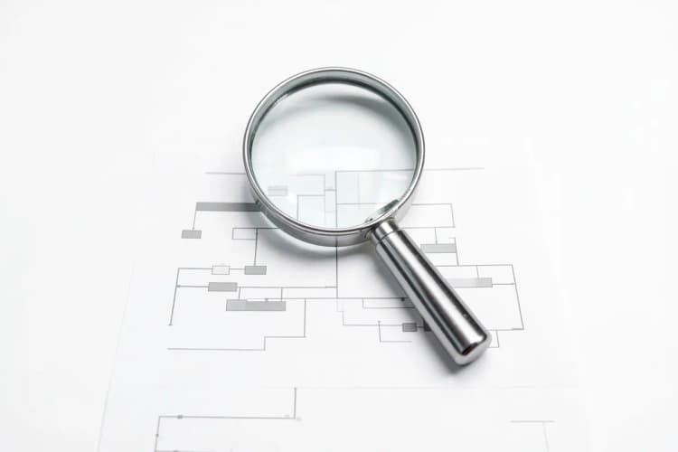 Uma lupa examinando cuidadosamente um diagrama de fluxo de processos de negócios, simbolizando a escolha do CRM ideal, sobre fundo branco.